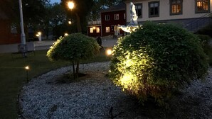 A courtyard with a statue, a red building, and a well-lit hedge. - Brunsbo G:a Biskopsgård Hotell & Konferens (Skara)