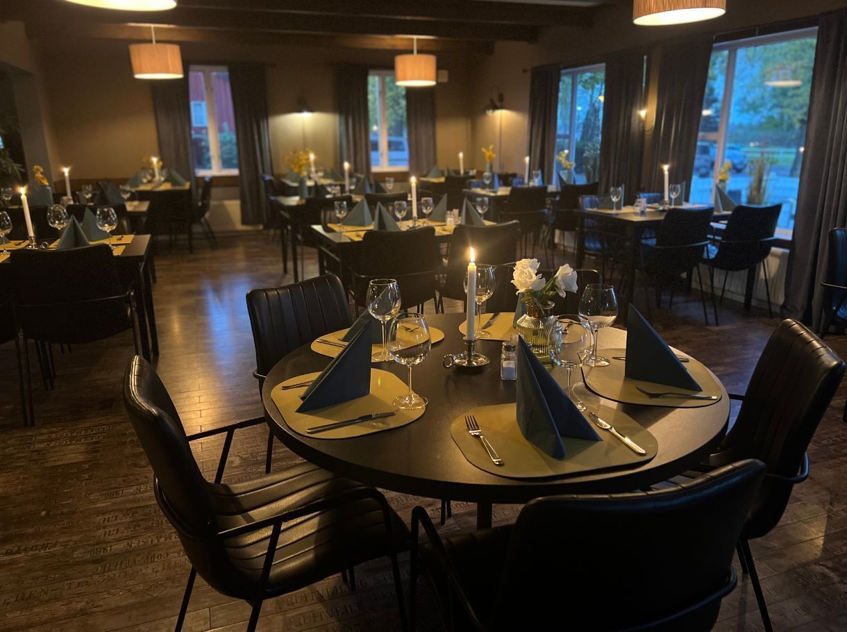 A restaurant with round tables set for dining, each with a candle, wine glasses, and cutlery.