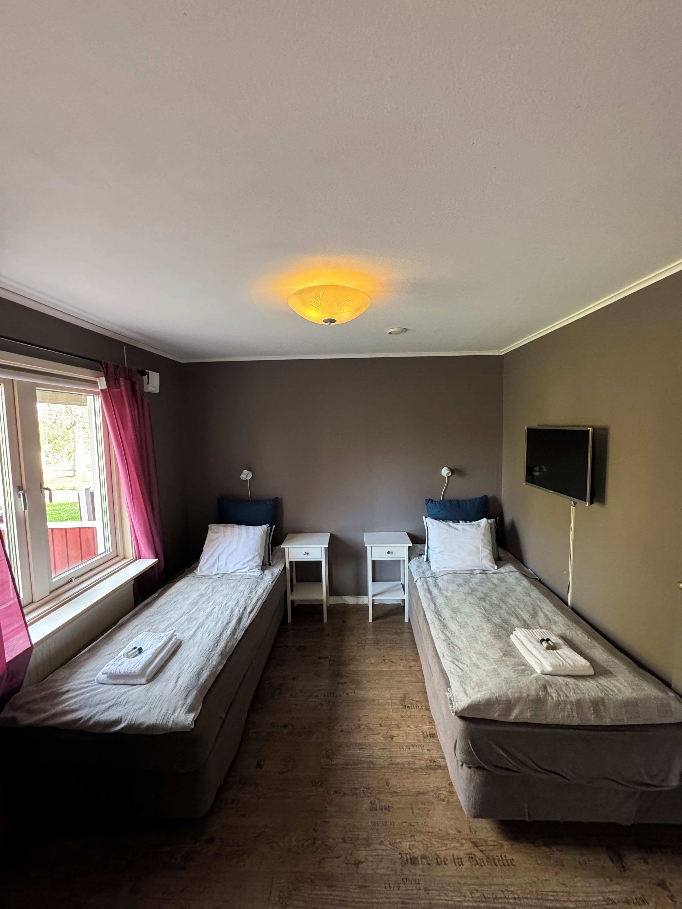 A room with two single beds, a small table, a TV, and a window with curtains.