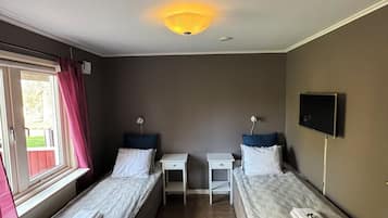 A room with two single beds, a small table, a TV, and a window with curtains.