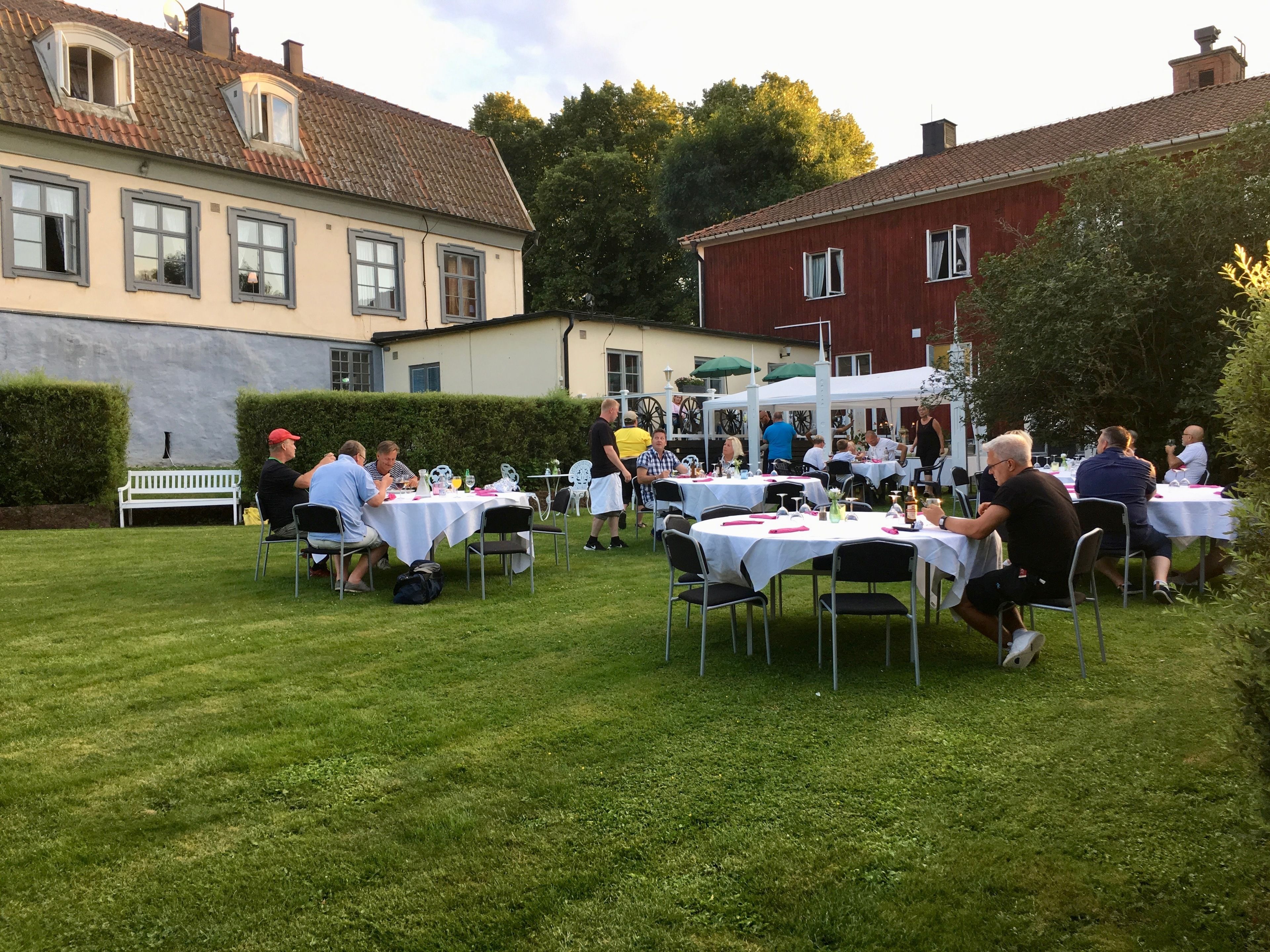 An outdoor event with tables set up on a grassy lawn, surrounded by buildings.