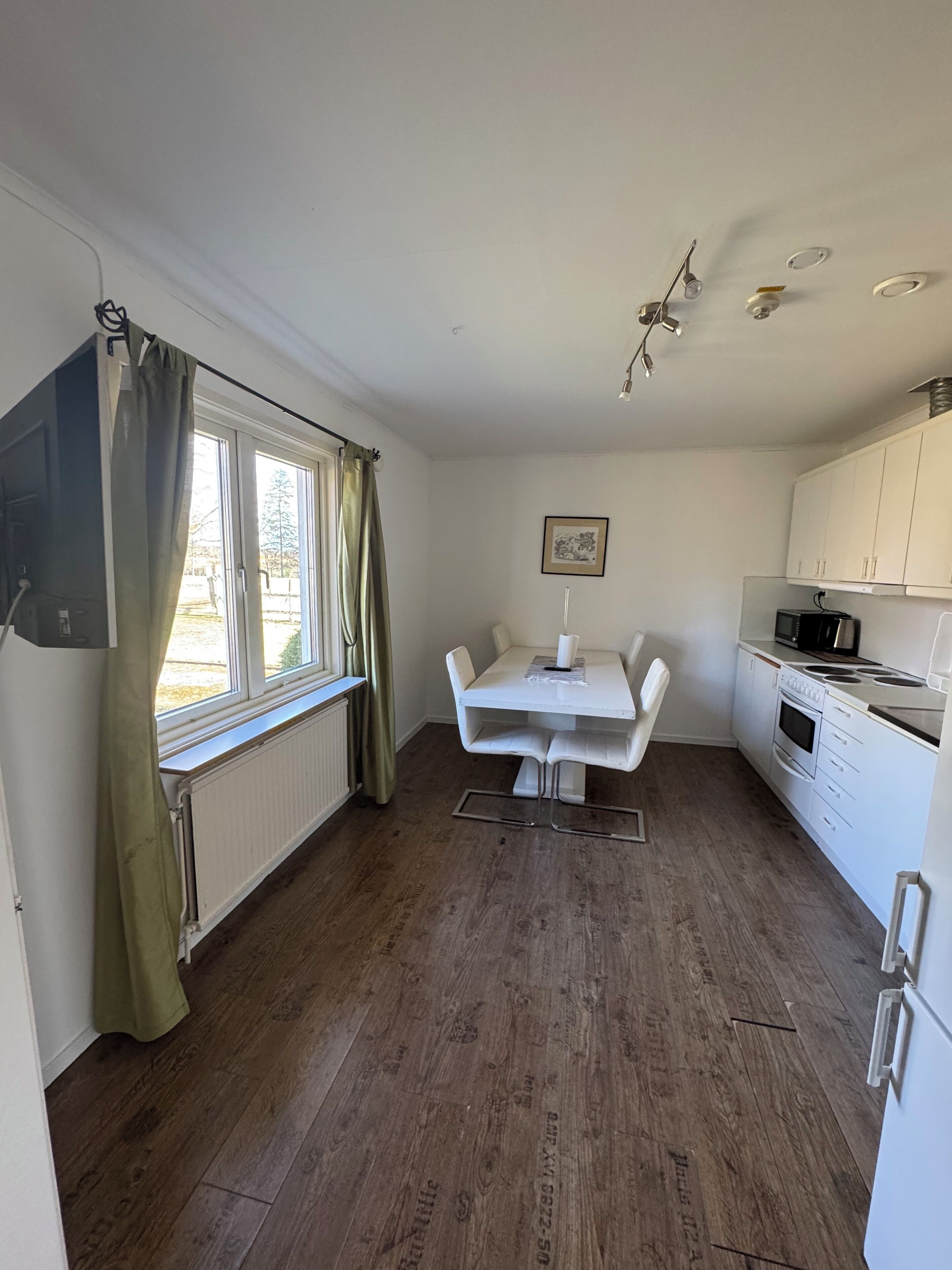 A compact kitchen with a dining table, white cabinets, and a window with curtains.