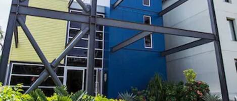 A modern building with a blue and yellow facade, surrounded by well-maintained greenery.