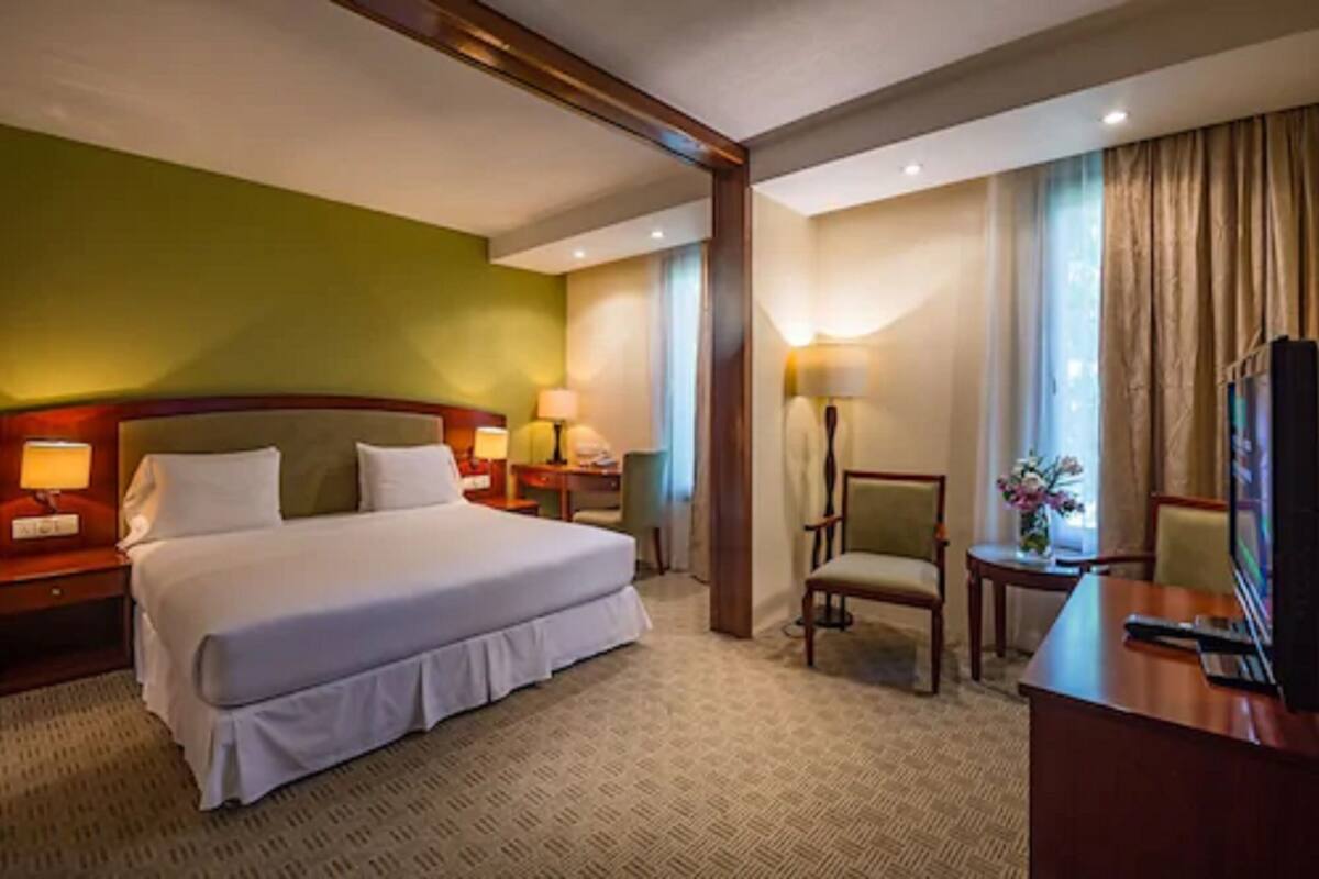 Ein Hotelzimmer mit einem großen Bett, Nachttischen mit Lampen, einem Schreibtisch mit Stuhl und einem Fernseher.