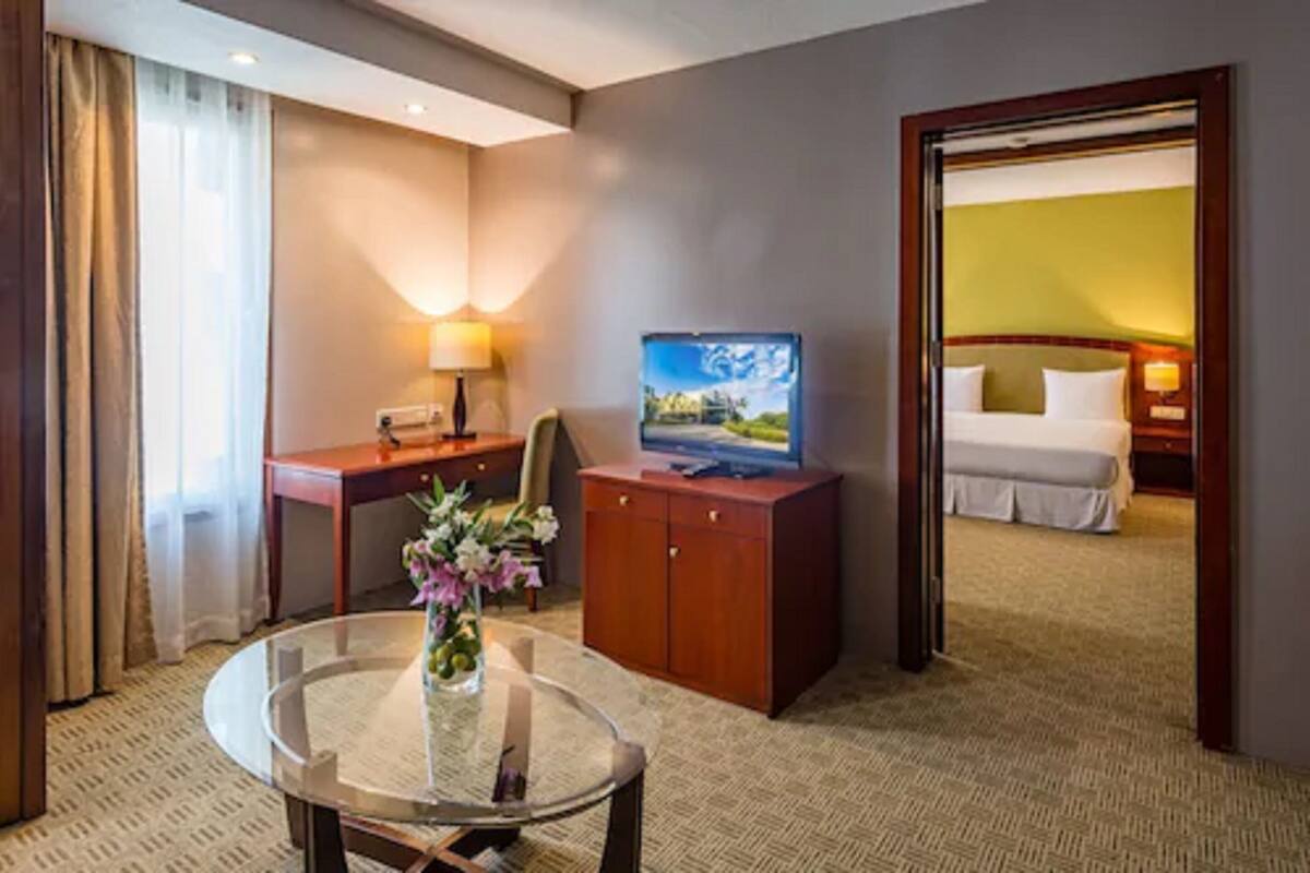 Ein Hotelzimmer mit einem Bett, einem Schreibtisch mit Lampe, einem Fernseher und einem Glastisch mit einer Vase.