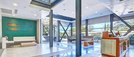 Un vestíbulo amplio con techo alto, ventanas grandes y un mostrador de recepción.