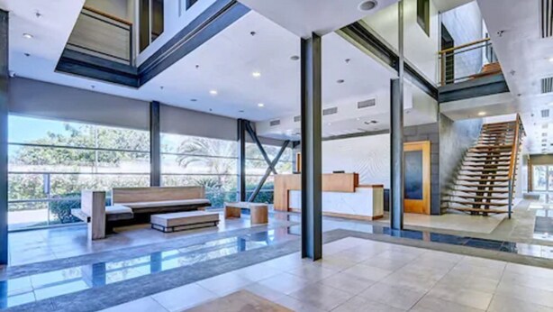 A spacious lobby with a modern design, featuring a central seating area, a staircase, and large windows offering a view of the outdoors. - Servotel (Port-au-Prince)