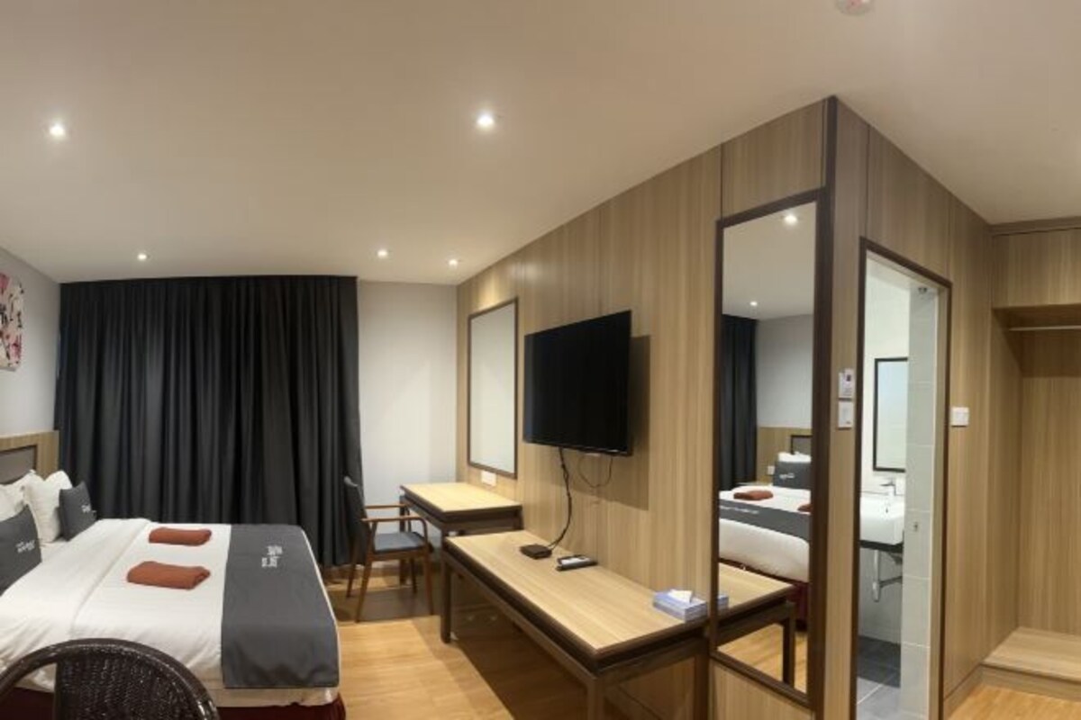 A hotel room with a bed, desk, chair, TV, and a mirror.