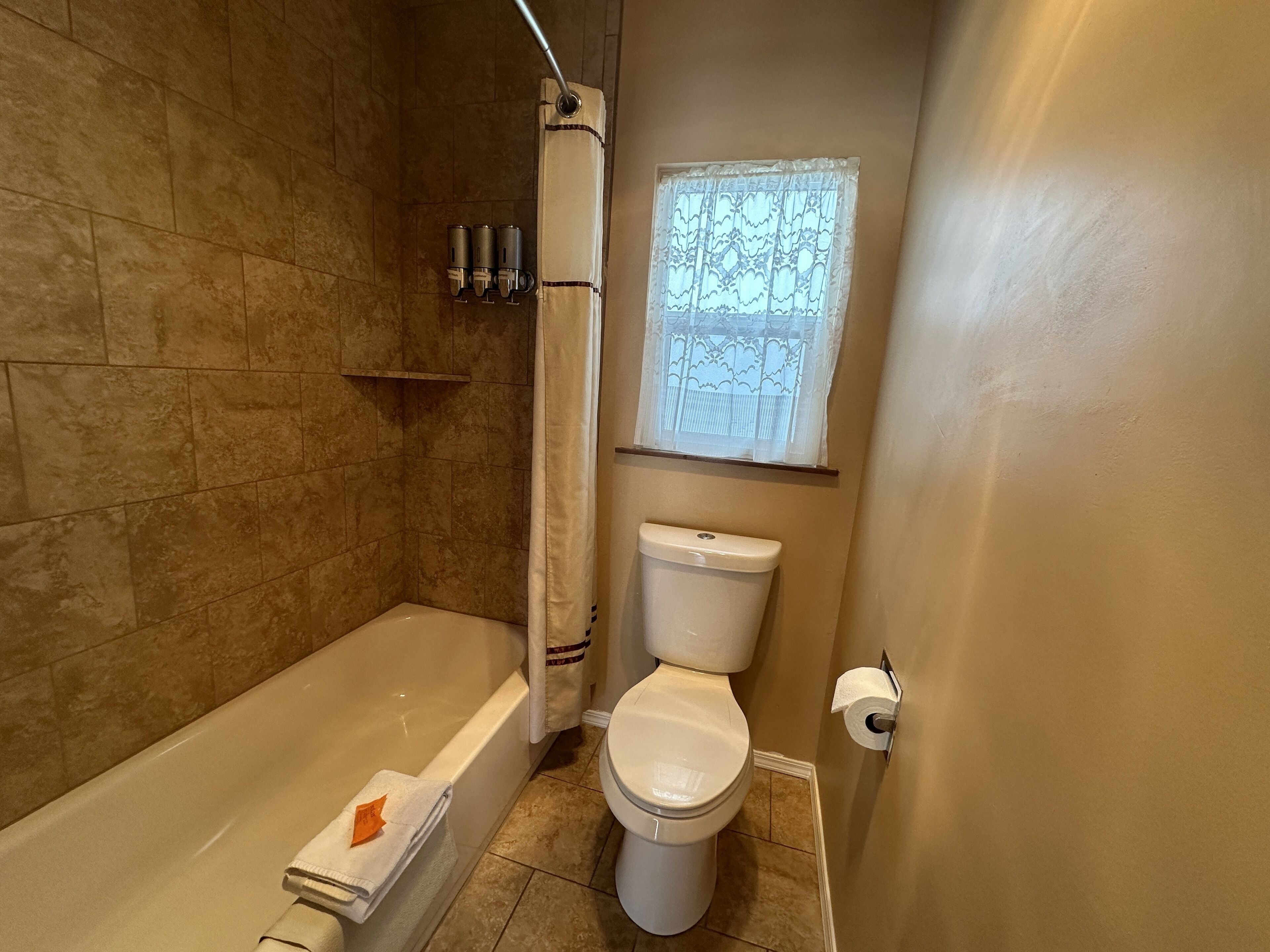 Ein Badezimmer mit Badewanne, Toilette und einem Fenster mit dekorativem Vorhang.