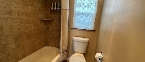 Ein Badezimmer mit Badewanne, Toilette und einem Fenster mit dekorativem Vorhang.