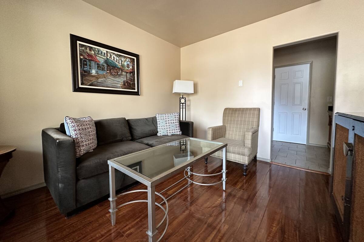 A living room with a dark grey sofa, a glass coffee table, a plaid armchair, and a framed picture on the wall.