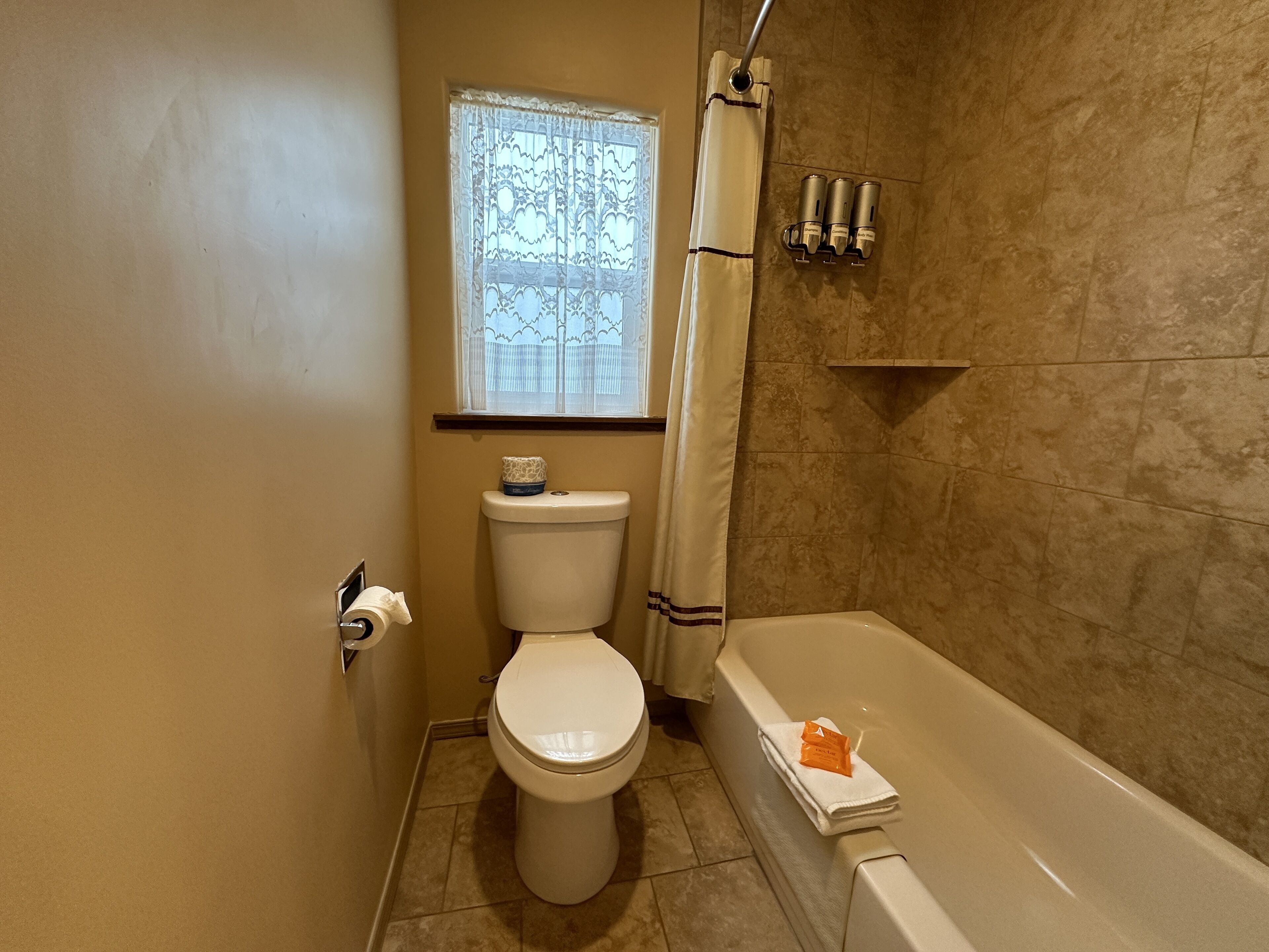 Un baño con inodoro, una ventana con cortina, ducha y bañera.