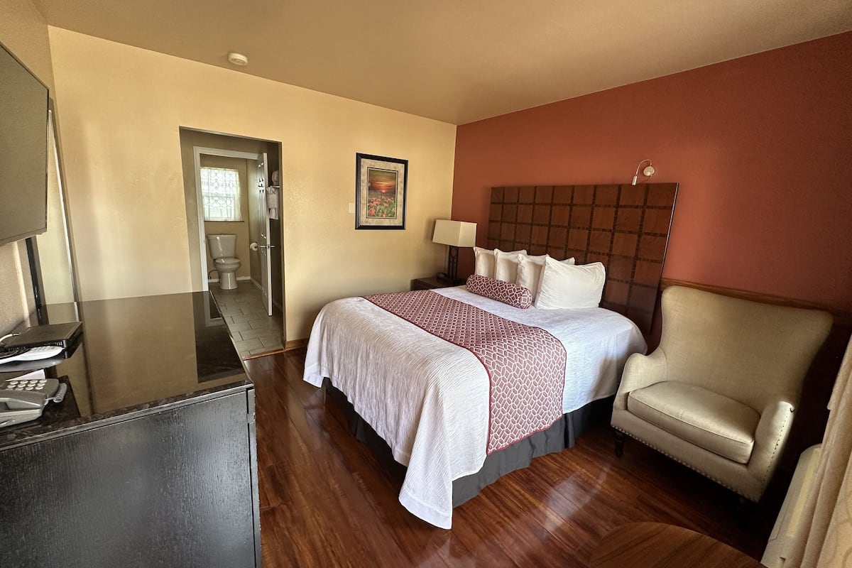 A hotel room with a bed, a desk, a chair, and a bathroom visible through an open door.