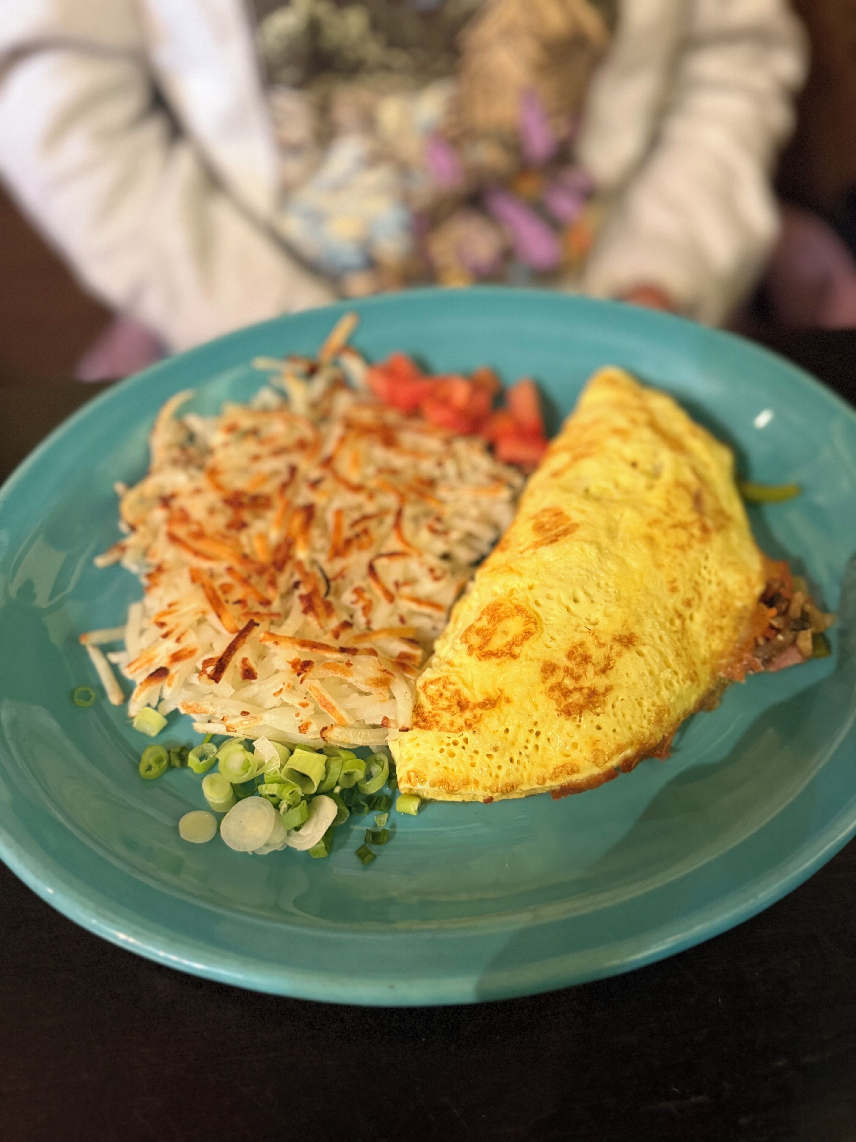Un piatto con un'omelette, patate sfilacciate e cipollotti.