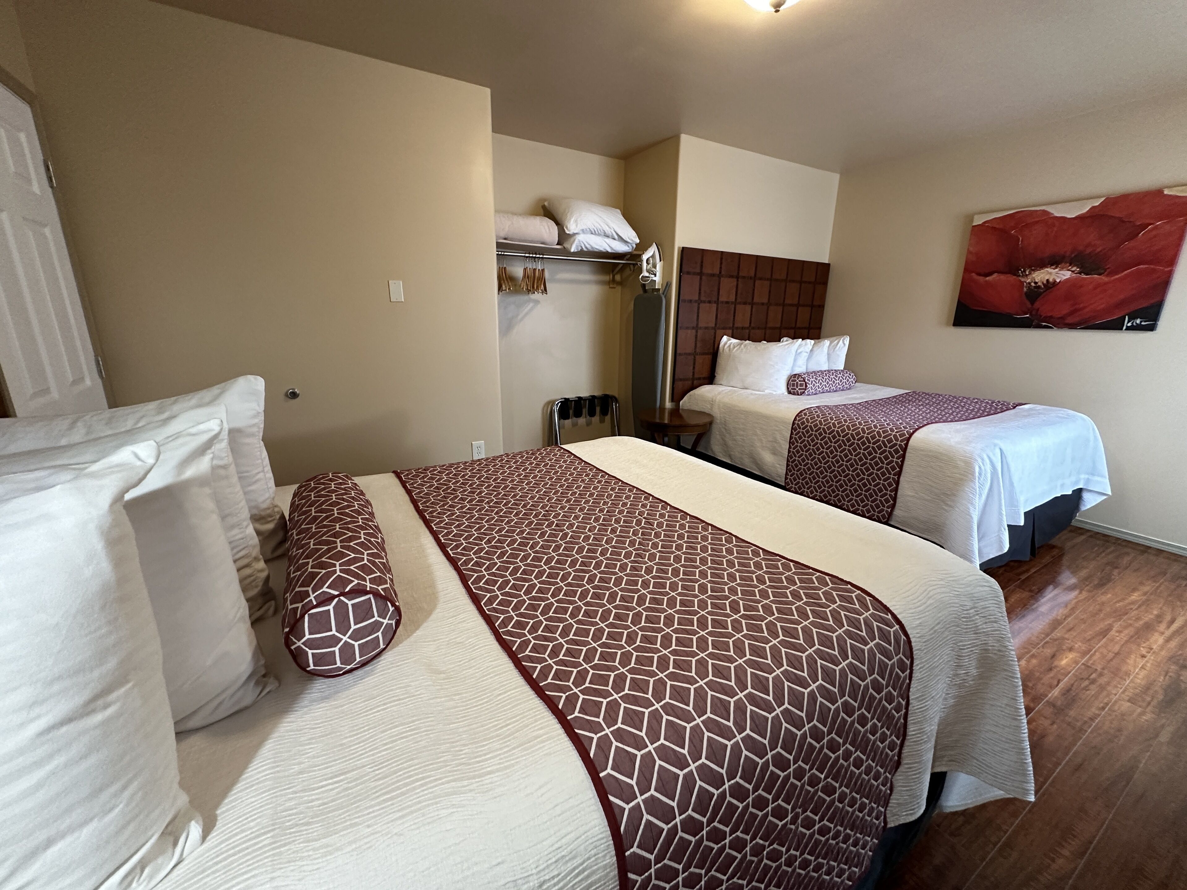 Habitación de hotel con dos camas, cada una con ropa de cama y almohadas estampadas, cabecero, una mesita y un cuadro de una flor roja en la pared.