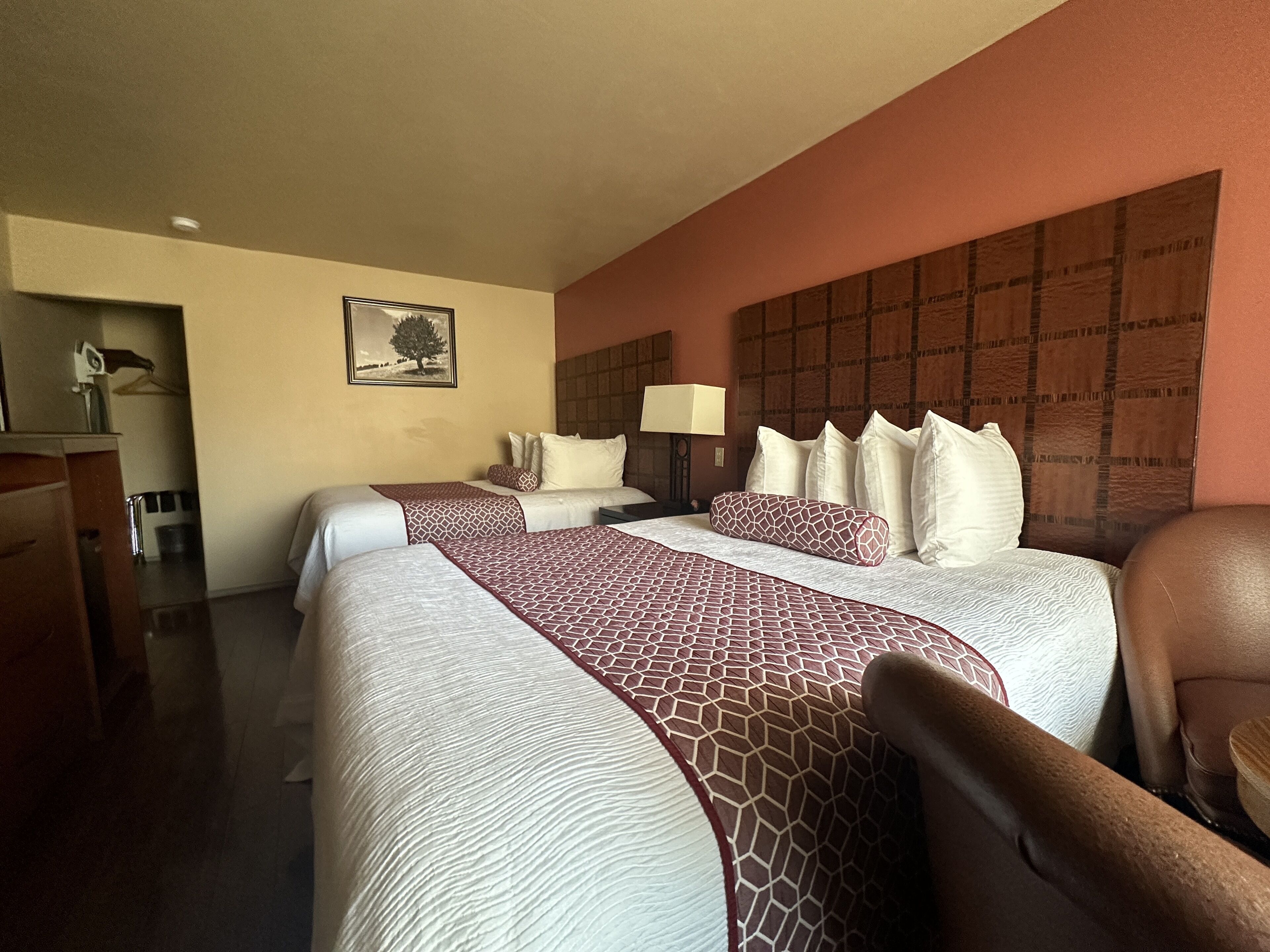 A hotel room with two beds, a desk, a chair, a lamp, and a painting on the wall.