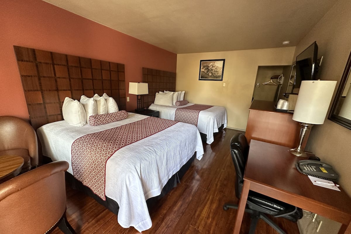 A hotel room with two beds, a desk, a chair, a desk lamp, a telephone, and a mirror.