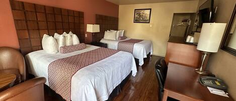 A hotel room with two beds, a desk, a chair, a desk lamp, a telephone, and a mirror.
