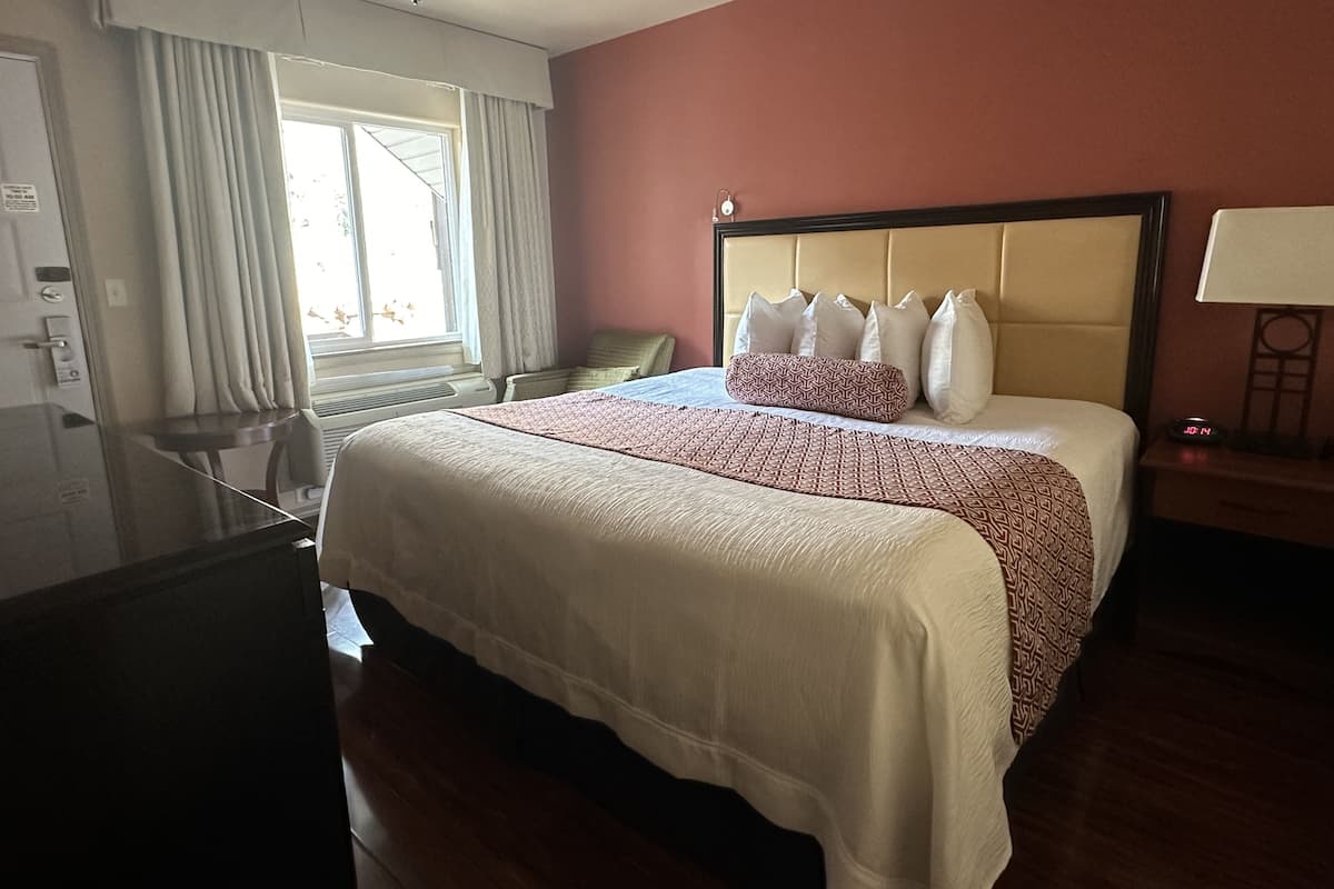 A hotel room with a large bed, a desk, and a window with curtains.