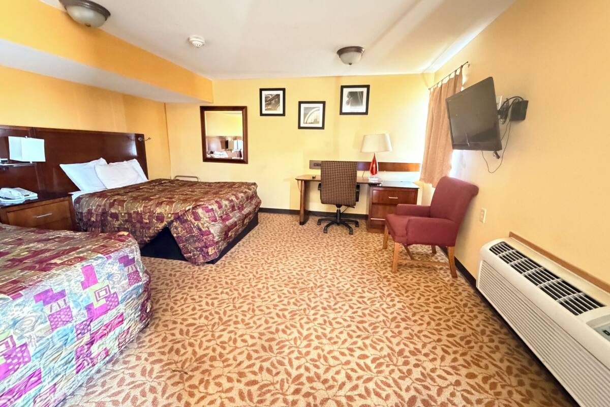 Habitación de hotel con dos camas, un escritorio, una silla, un televisor y un calentador.