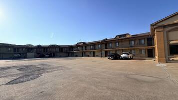 A multi-story motel with a parking lot, several cars parked, and a clear blue sky.