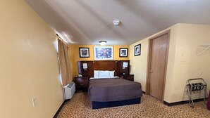 A hotel room with a patterned carpet, a bed with a headboard, a bedside table with a lamp, a heater, and a wardrobe.