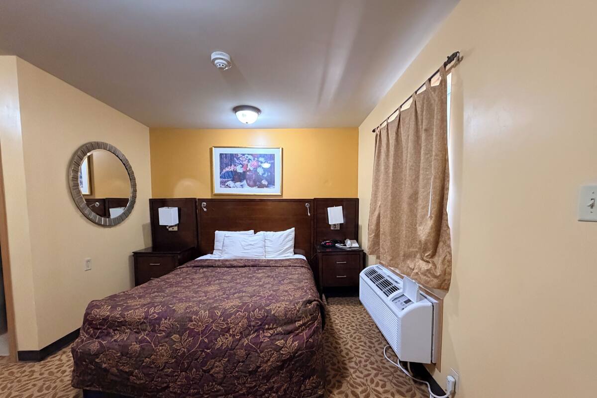 Habitación de hotel con una cama grande, un espejo redondo, un ventilador de techo y un cuadro en la pared.