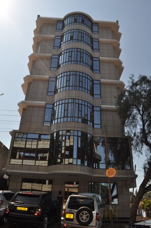 Un edificio de varios pisos con fachada curva, amplias ventanas y un estacionamiento con varios coches.