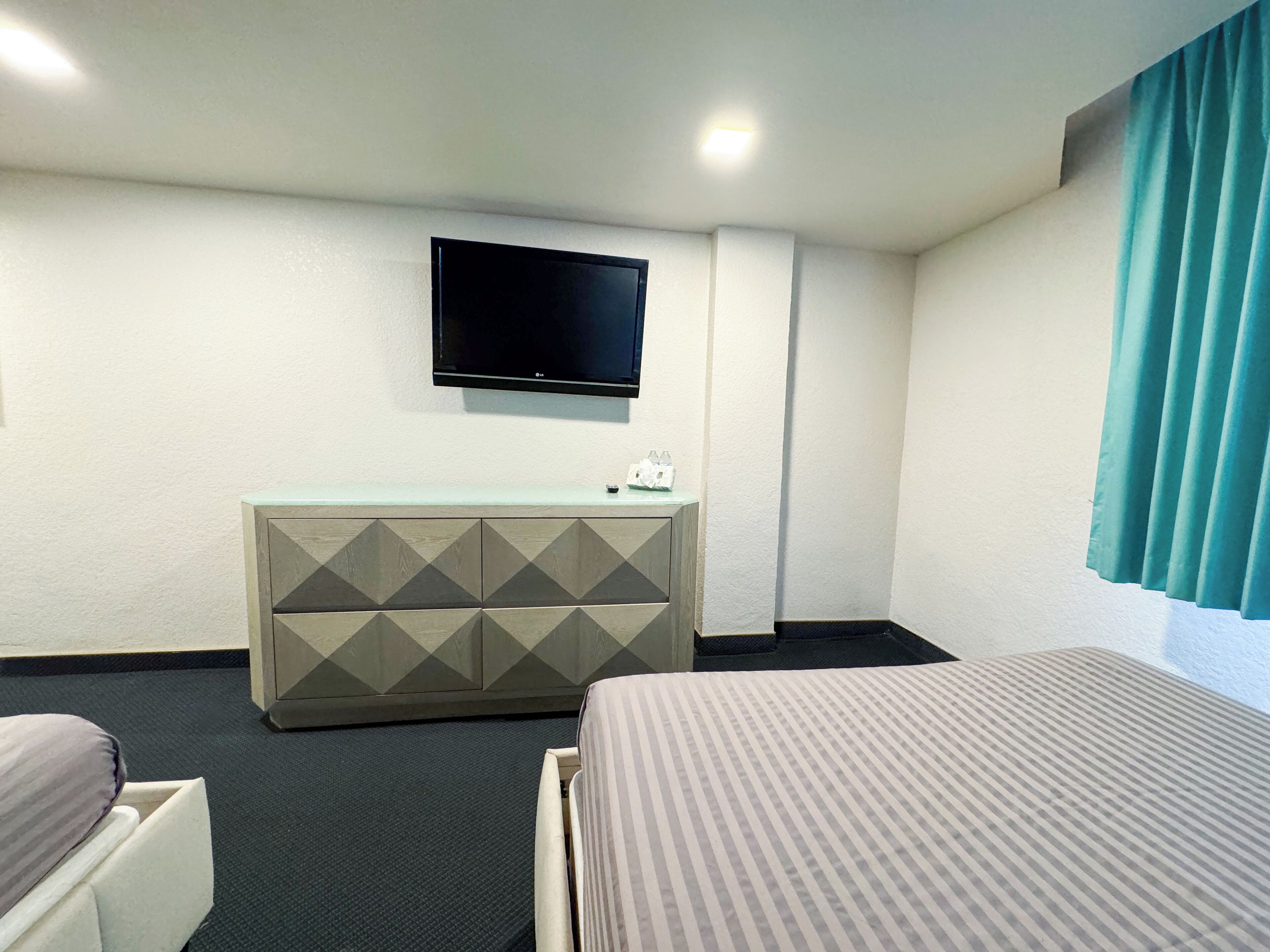 Habitación de hotel con cama, un escritorio pequeño con televisor de pantalla plana y ventana con cortinas.