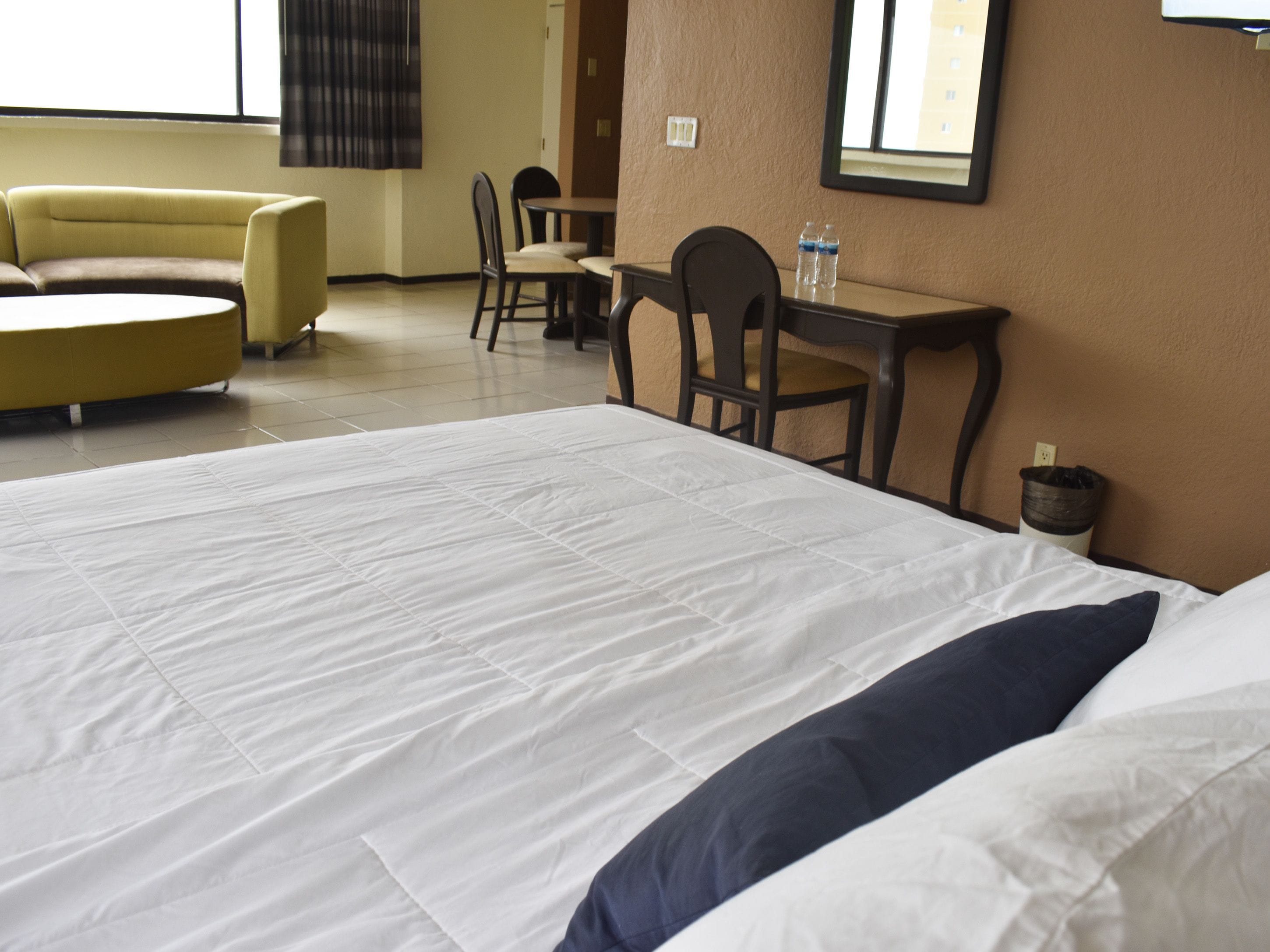 Habitación de hotel con una cama grande, un sofá, una mesa de comedor con sillas y un cubo de basura pequeño.