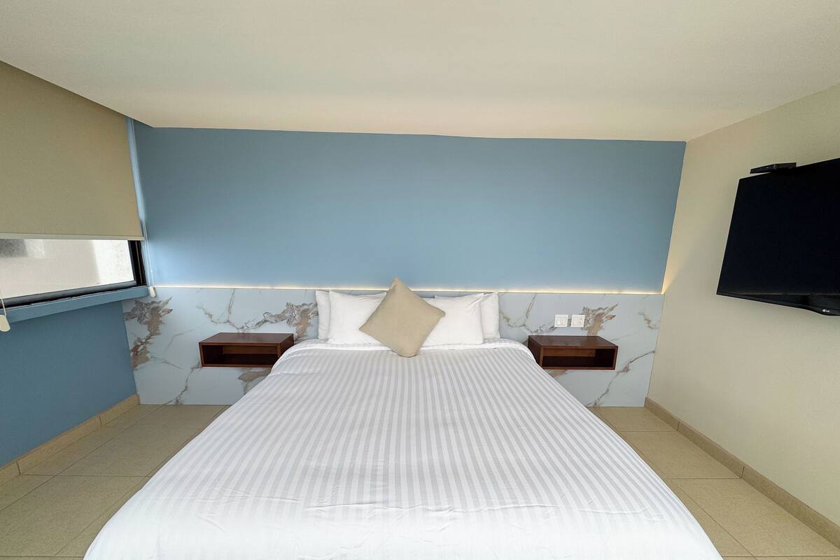 A hotel room with a large bed, two bedside tables, a TV mounted on the wall, and a marble-patterned wall.