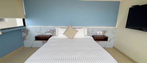 A hotel room with a large bed, two bedside tables, a TV mounted on the wall, and a marble-patterned wall.