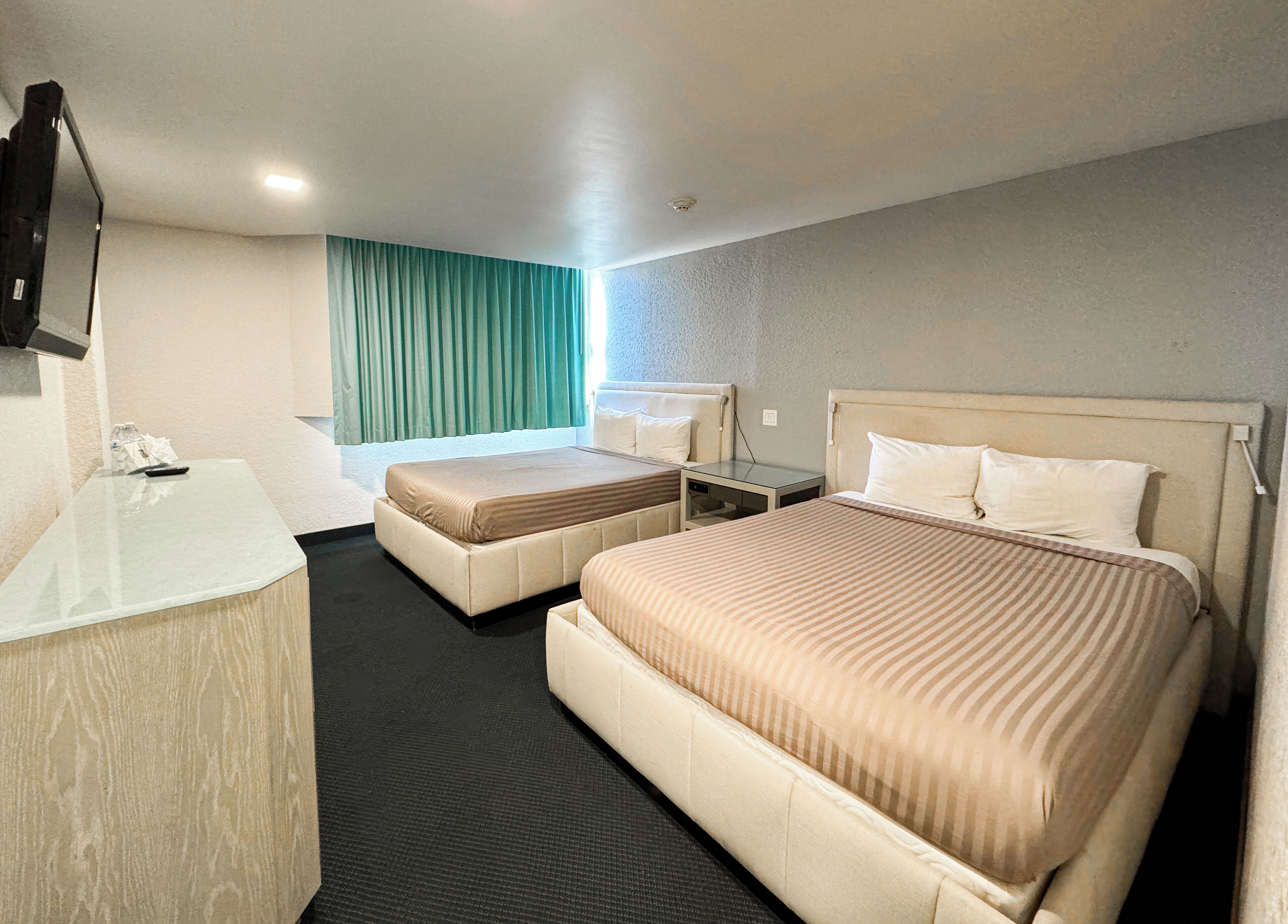 A hotel room with two beds, a desk, and a mirror.
