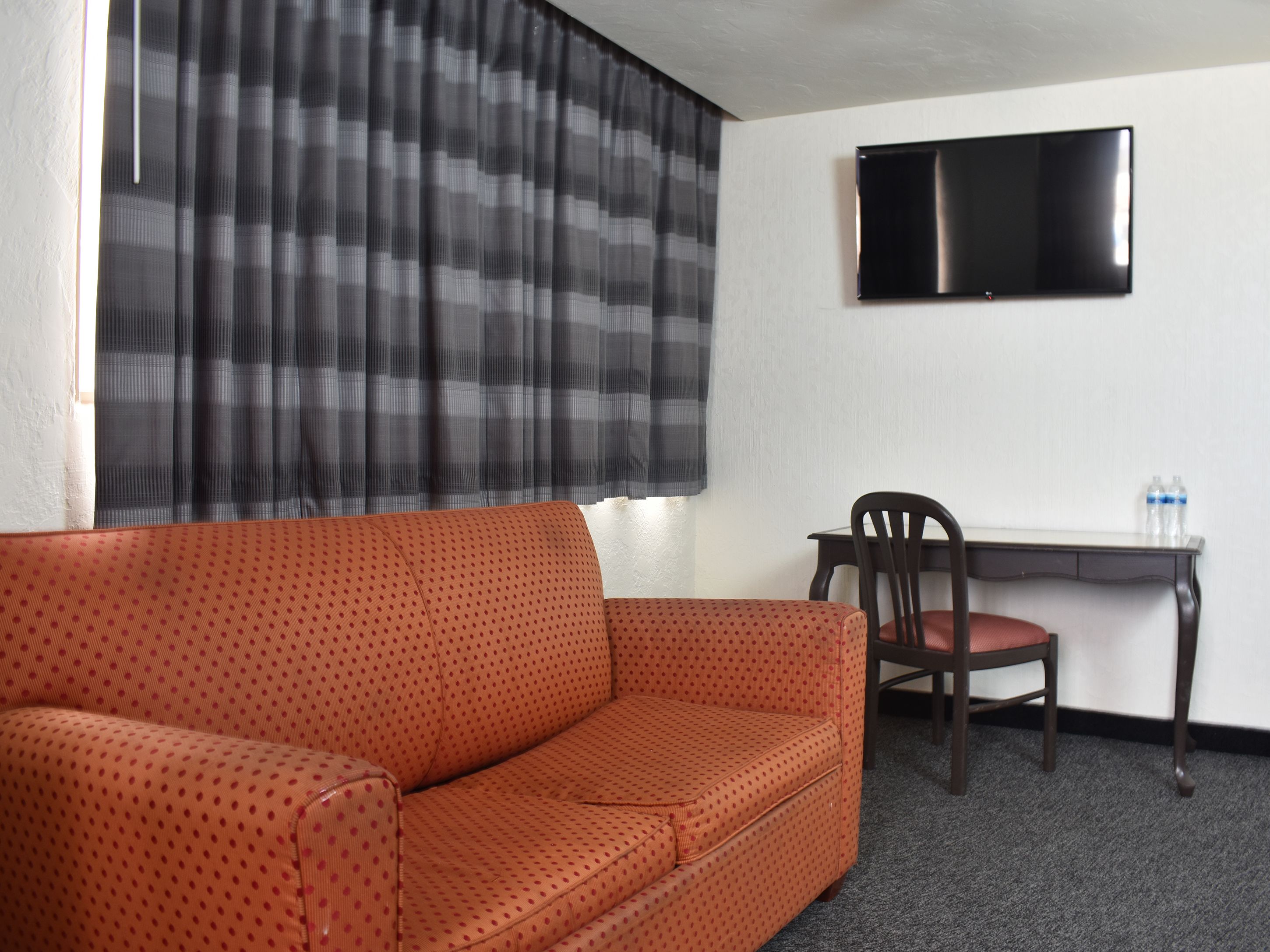 Une pièce avec un canapé rouge à pois, un bureau en bois foncé, une chaise et un téléviseur à écran plat fixé au mur.