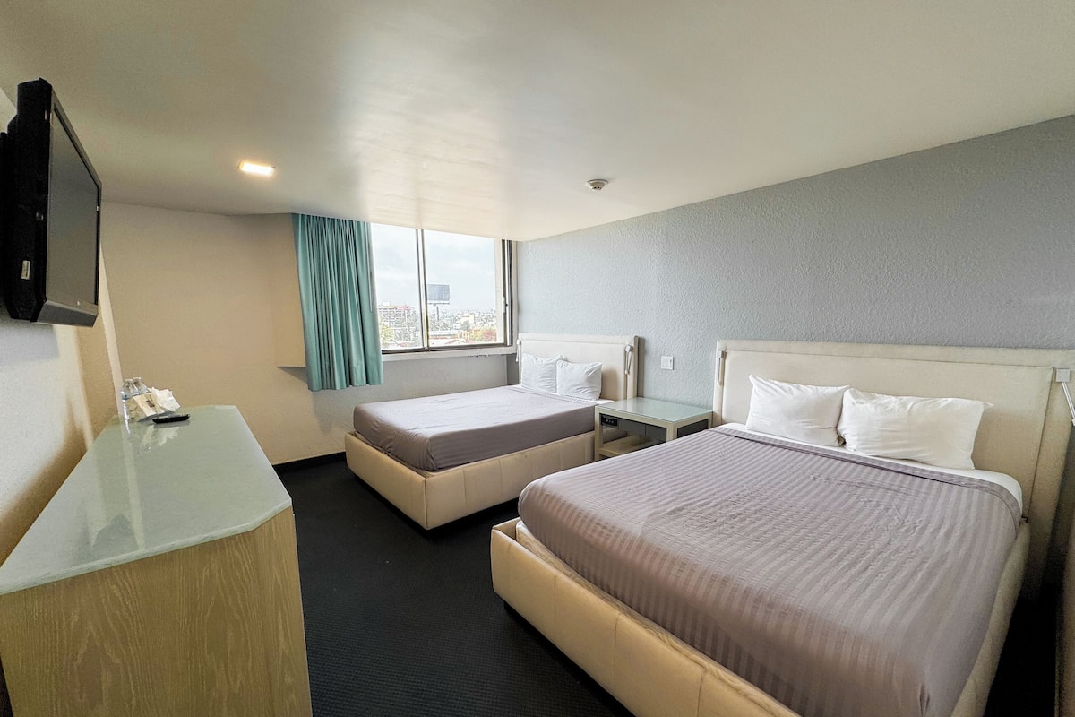 A hotel room with two beds, a desk, a television, and a window with curtains.