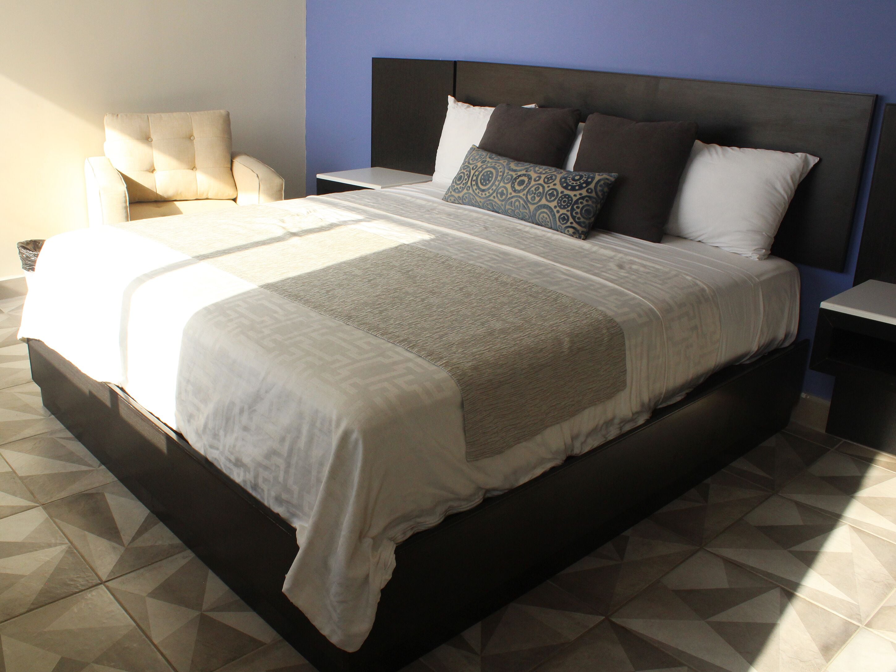 Una cama grande con cabecera oscura, varios cojines y una colcha estampada.