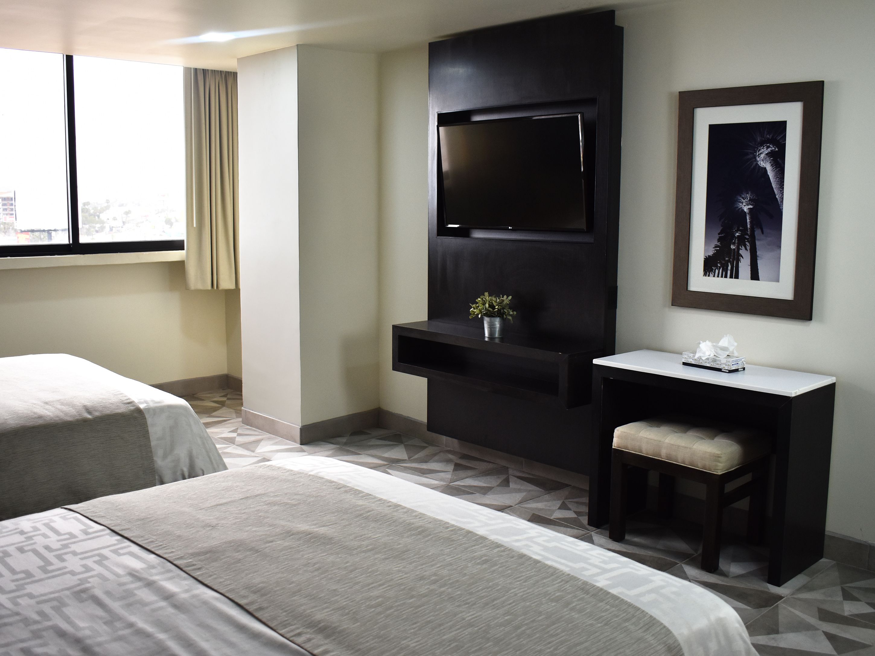Quarto de hotel com duas camas, uma televisão de tela plana na parede, uma pequena escrivaninha com cadeira e um quadro na parede.