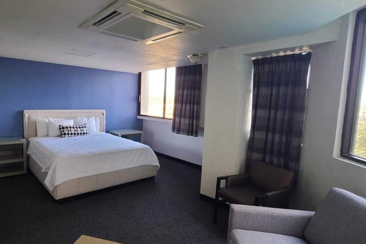 A hotel room with a bed, a chair, a desk, and a window with curtains.