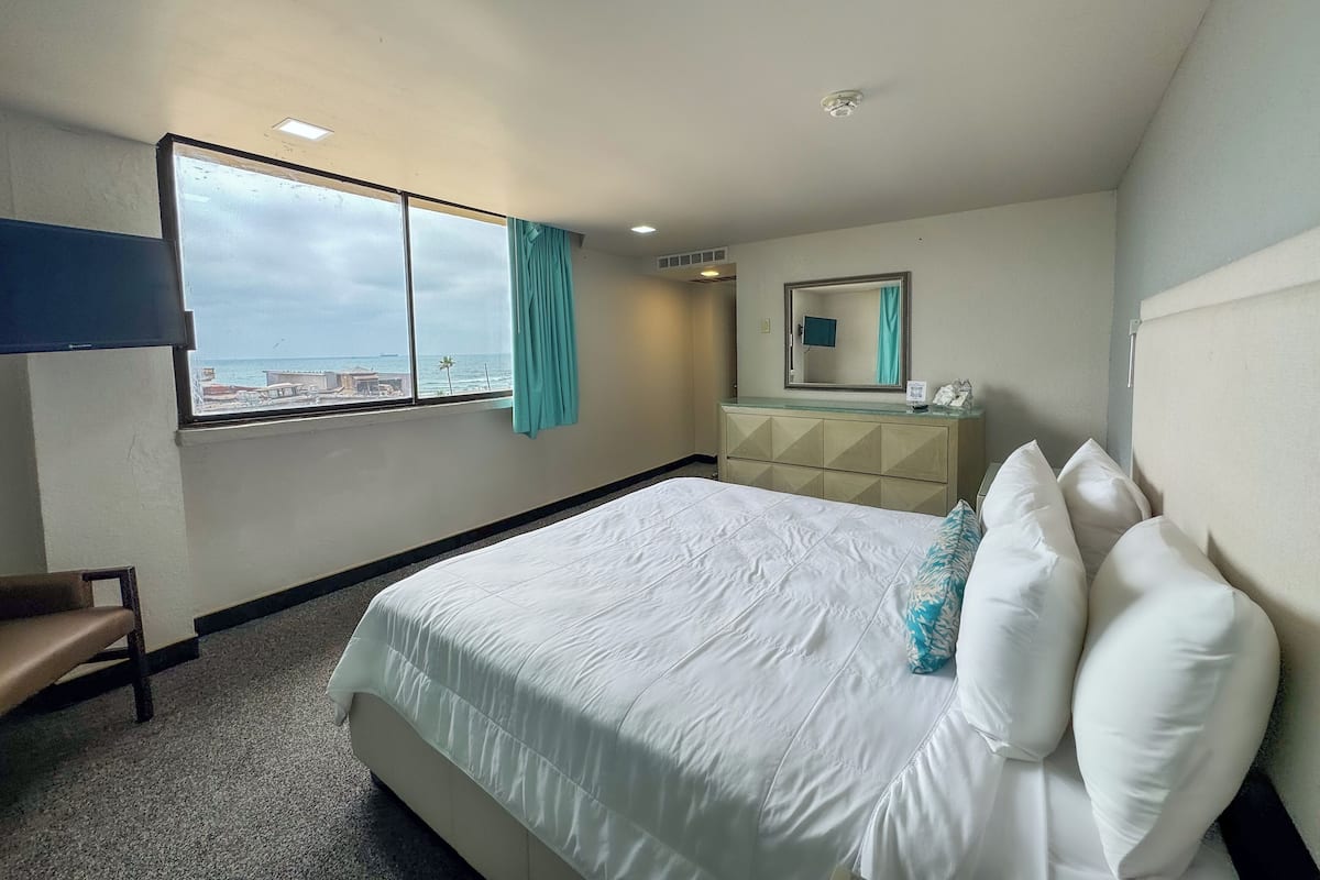 A hotel room with a bed, a dresser, a mirror, and a window with a view of the sea.