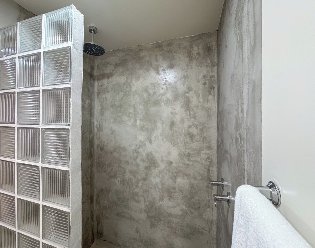 Ducha con pared texturizada, puerta de cristal y barra para toallas.