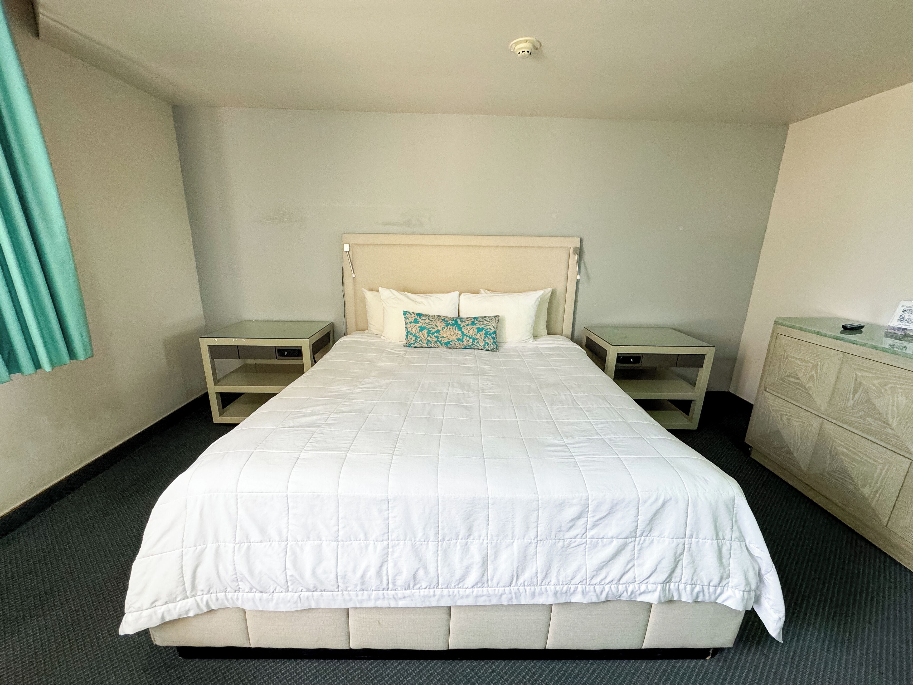A hotel room with a large bed, two bedside tables, a dresser, and a ceiling light.