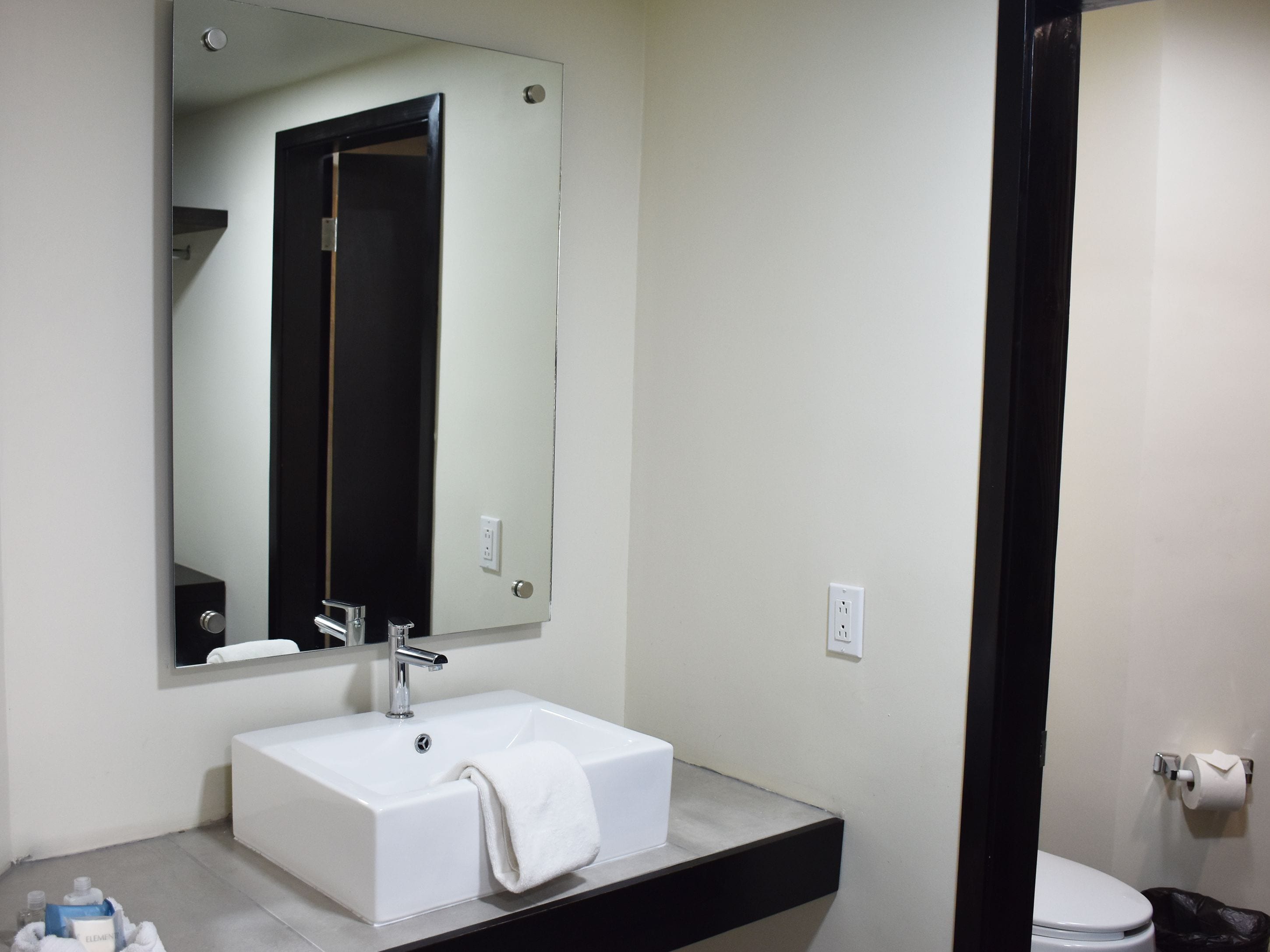 Une salle de bain moderne avec un lavabo blanc, un grand miroir et une porte à cadre noir.