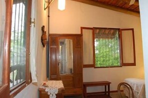 Una habitación con puerta de madera, una mesa pequeña con mantel de encaje, un banco y una ventana con cortinas.
