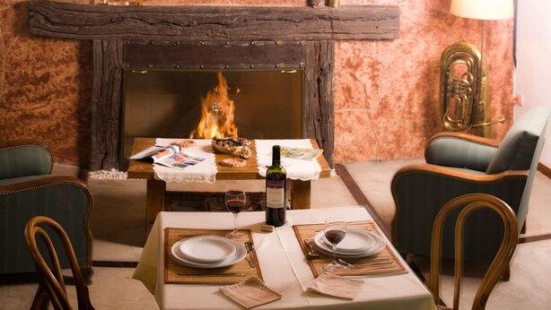 A cozy dining area with a fireplace, wooden chairs, a table set for two with plates, glasses, and a bottle of wine. - Golden Lodge (Paso de la Patria)