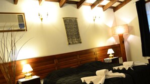 A hotel room with a wooden headboard, a bed with dark bedding, a wall-mounted air conditioner, a decorative tapestry, and a bedside lamp. - Golden Lodge (Paso de la Patria)