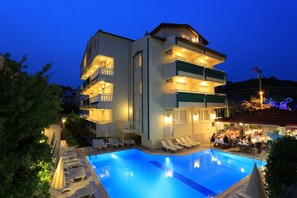 Un hotel moderno con piscina, varios balcones y zonas de estar al aire libre.