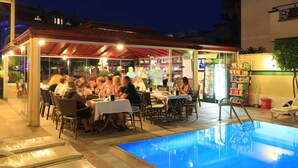 An outdoor pool area with tables and chairs, surrounded by a covered patio with a red roof. - Amaris Apartments (Marmaris)