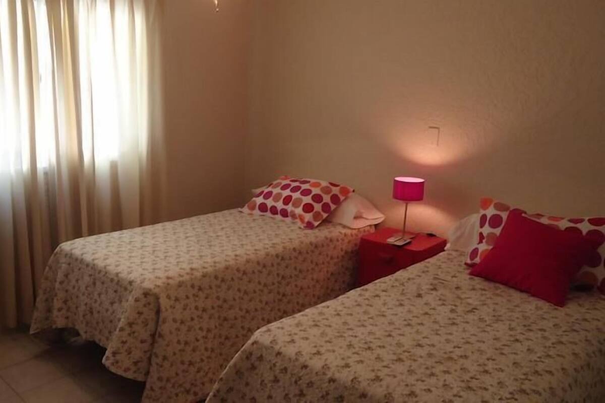 Una habitación con dos camas, cada una con una colcha estampada y almohadas a juego. Entre las camas, un mesita de noche con una lámpara.