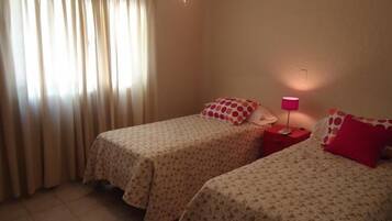 A room with two beds, each with a floral bedspread and matching pillows. There is a nightstand with a lamp between the beds.