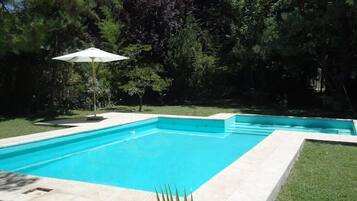 A rectangular swimming pool with a tiled edge, surrounded by a grassy area and trees.